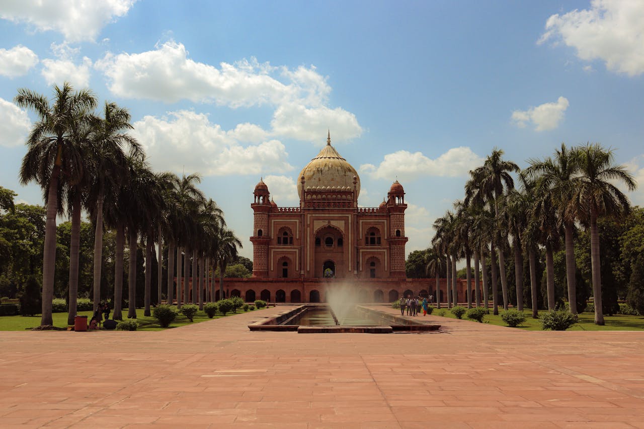 portfolio-img-03 A scenic view of Safdarjung Tomb in New Delhi with palm trees and a fountain under a bright blue sky.